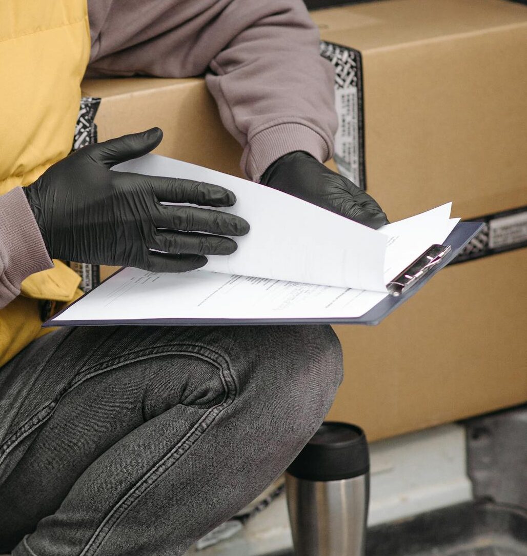Delivery courier reviewing documents with packages in a van, adhering to safety protocols.